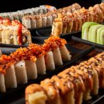 Close-up of colorful sushi rolls with diverse toppings on black plates, showcasing vibrant Japanese cuisine.