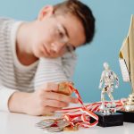 A thoughtful teenager sits by a table with various trophies and medals.